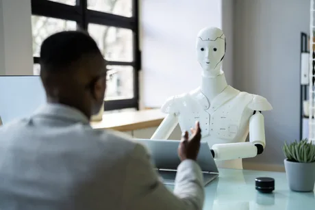 Un robot interacționează cu un bărbat la birou, discutând despre tehnologie.