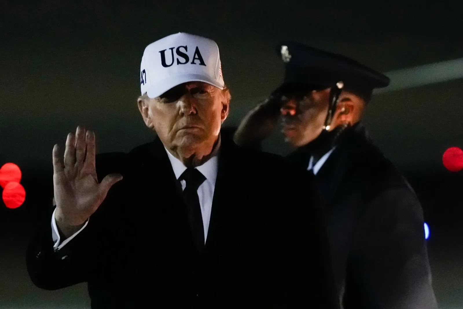 Donald Trump salută în fața unei mulțimi, purtând o șapcă albă.
