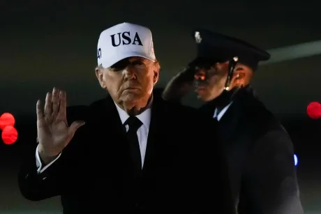 Donald Trump salută în fața unei mulțimi, purtând o șapcă albă.