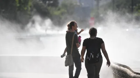 Persoane plimbându-se pe stradă într-o zi călduroasă, cu vapori de apă în jur.