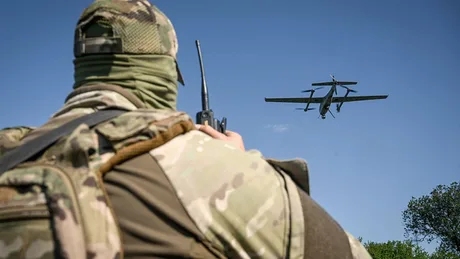 Un soldat observă o dronă zburând pe cerul albastru.