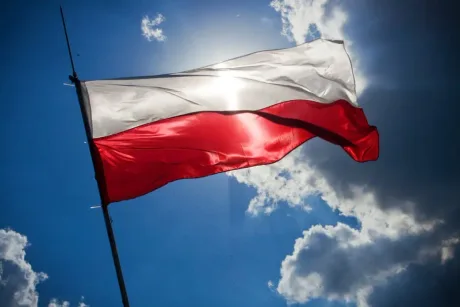 Steagul Poloniei fluturând sub soare pe un fundal albastru.