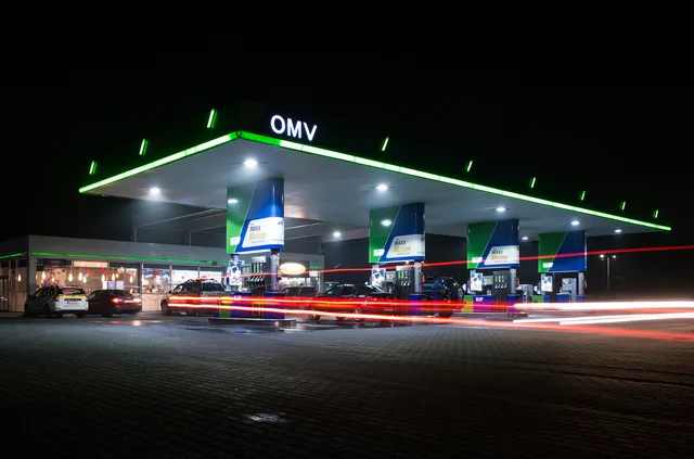 Benzinăria OMV iluminată noaptea, cu mașini la pompă.