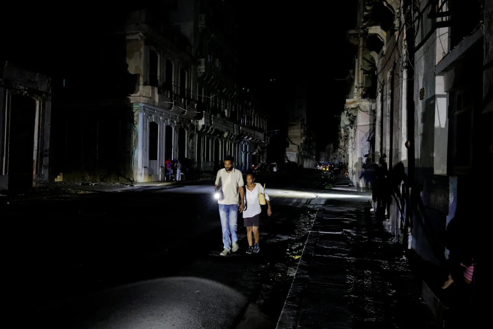 Oameni merg pe o stradă întunecată din Cuba, cu lanterne în mână.