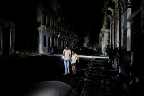 Oameni merg pe o stradă întunecată din Cuba, cu lanterne în mână.