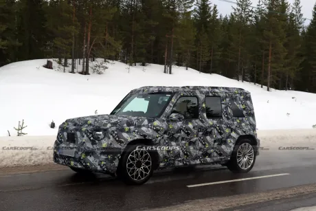 Un vehicul camuflat pe un drum de munte, înconjurat de zăpadă și copaci verzi.