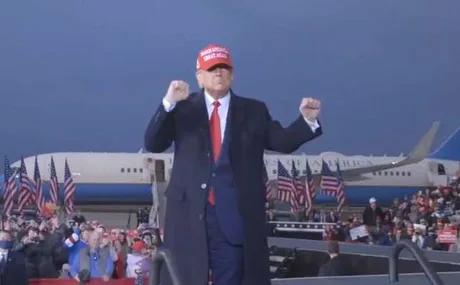 Donald Trump vorbește la un eveniment cu steaguri americane în fundal.