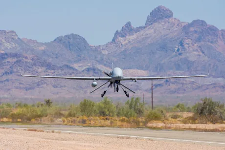 Dronă militară în zbor, pe fundalul unui peisaj montan arid.