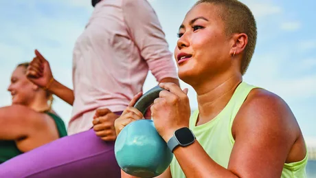 Femeie cu kettlebell, antrenament în aer liber, smartwatch pe mână.
