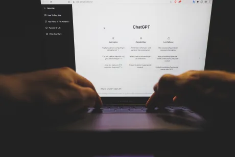 Ecran de laptop cu interfața ChatGPT deschisă, mâini pe tastatură.