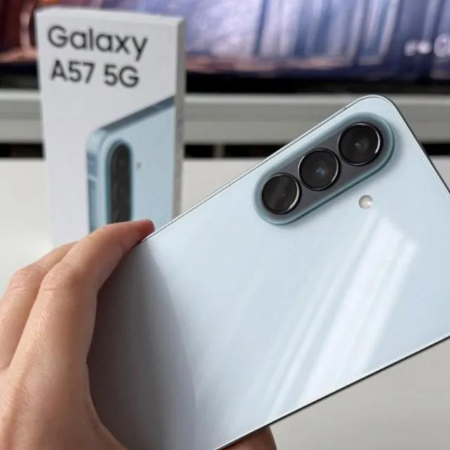 Samsung Galaxy A57 cu camera și cutie în fundal.
