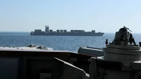 Nava cargo navigând pe mare, cu un peisaj calm în fundal.