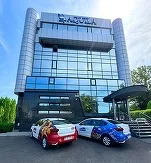 Clădire modernă cu mașini parcate în față, soare strălucitor.