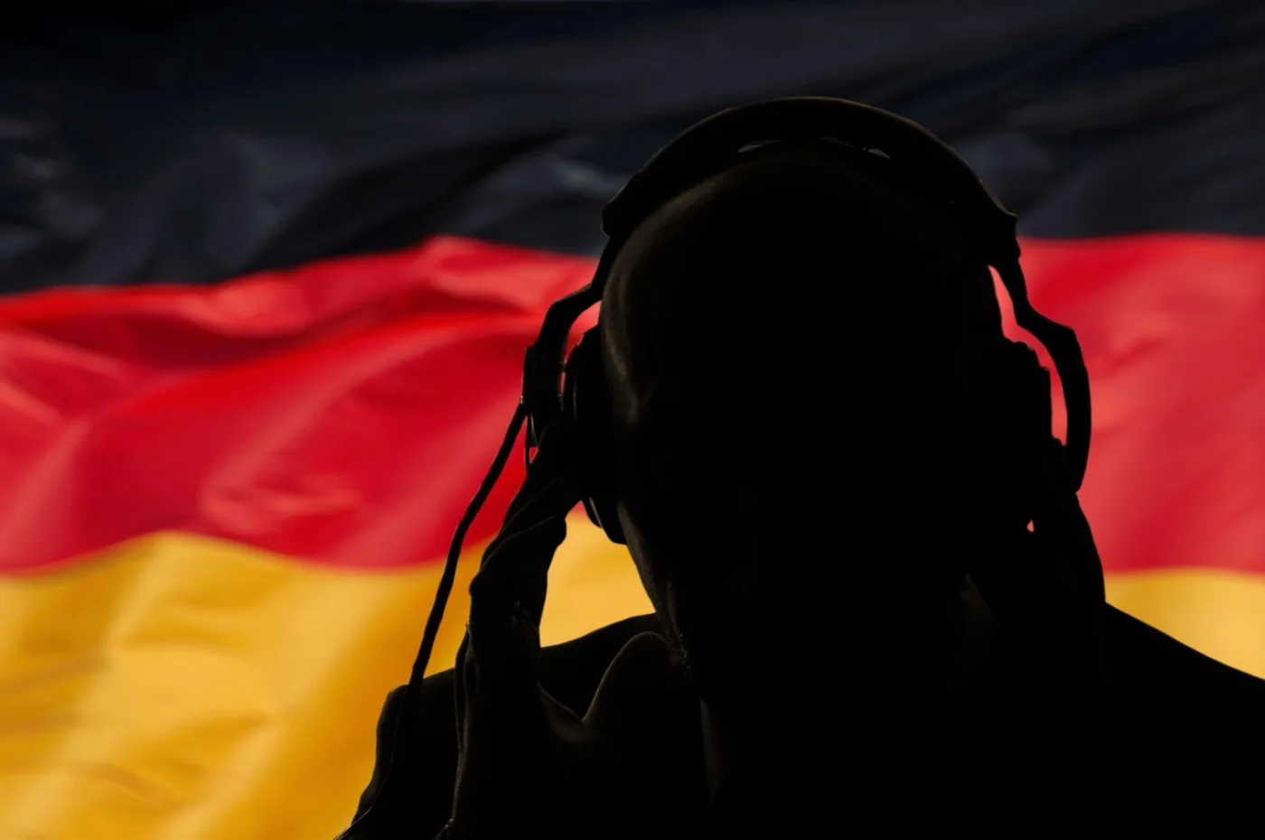 Silhouette de bărbat cu căști, pe fundalul steagului Germaniei.