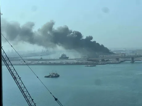 Fum negru de la o explozie în port, cu nave în fundal.