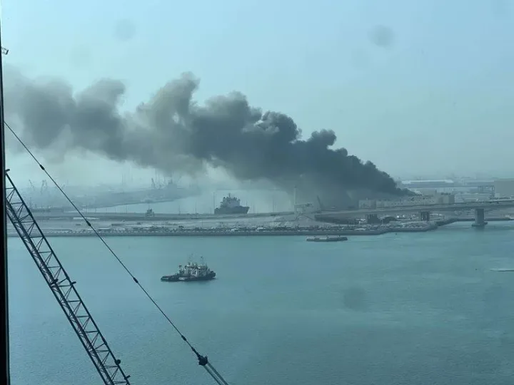 Fum negru de la o explozie în port, cu nave în fundal.