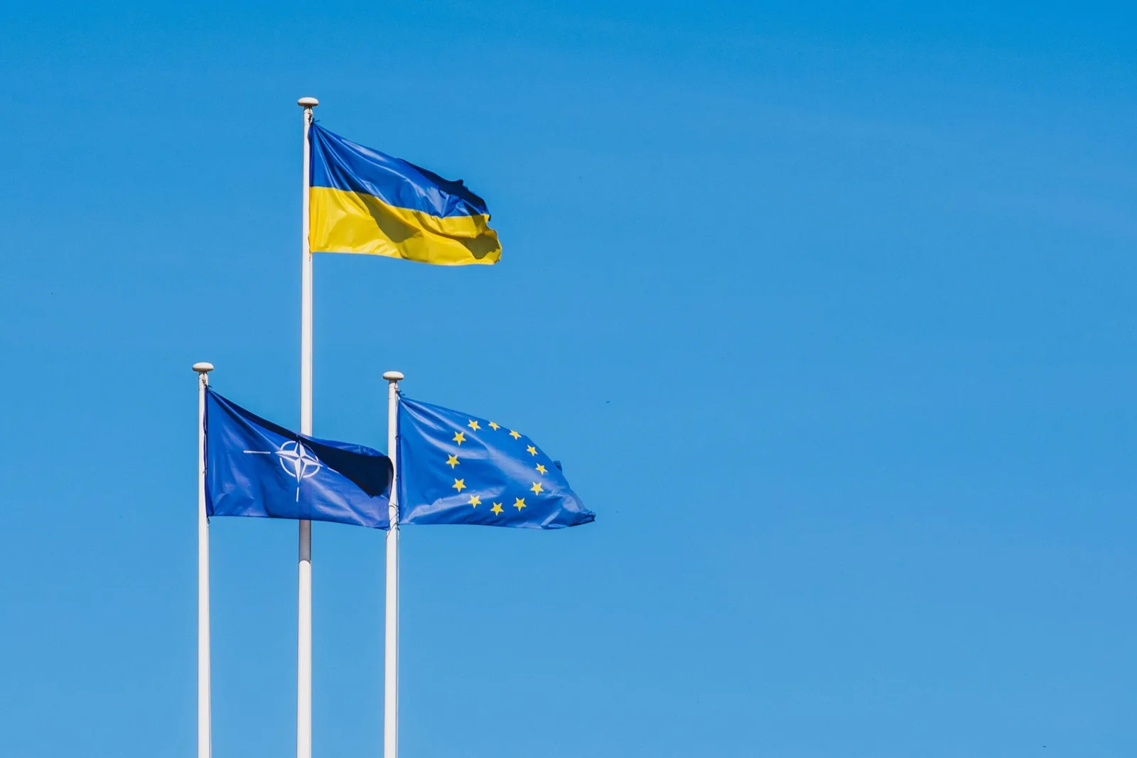 Steagurile Ucrainei, Uniunii Europene și NATO fluturând împreună pe fundal albastru.