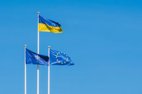 Steagurile Ucrainei, Uniunii Europene și NATO fluturând împreună pe fundal albastru.