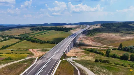 Peisaj cu autostradă recent construită, înconjurată de natură verde și dealuri.