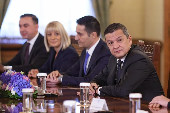 Discuții între lideri politici la o masă, cu flori și apă pe birou.