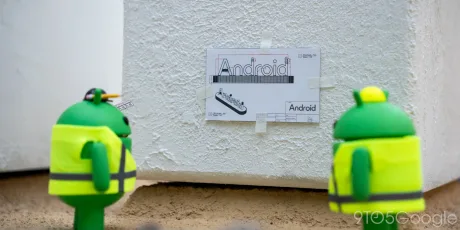 Doi roboți Android discută despre un afiș cu denumirea Android pe un perete.