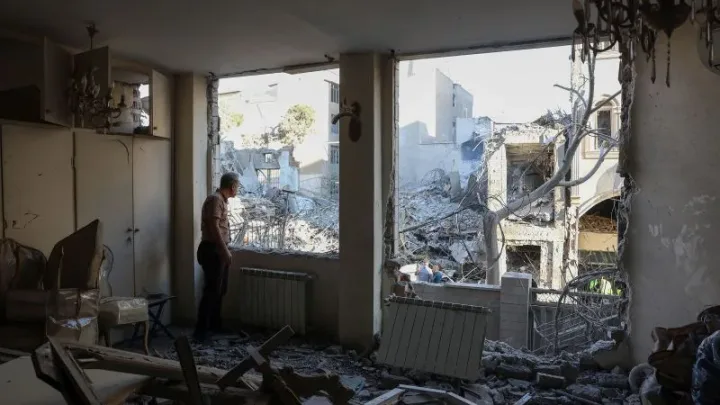 Un bărbat contemplând distrugerea unei clădiri, cu feronerie și moloz în jur.