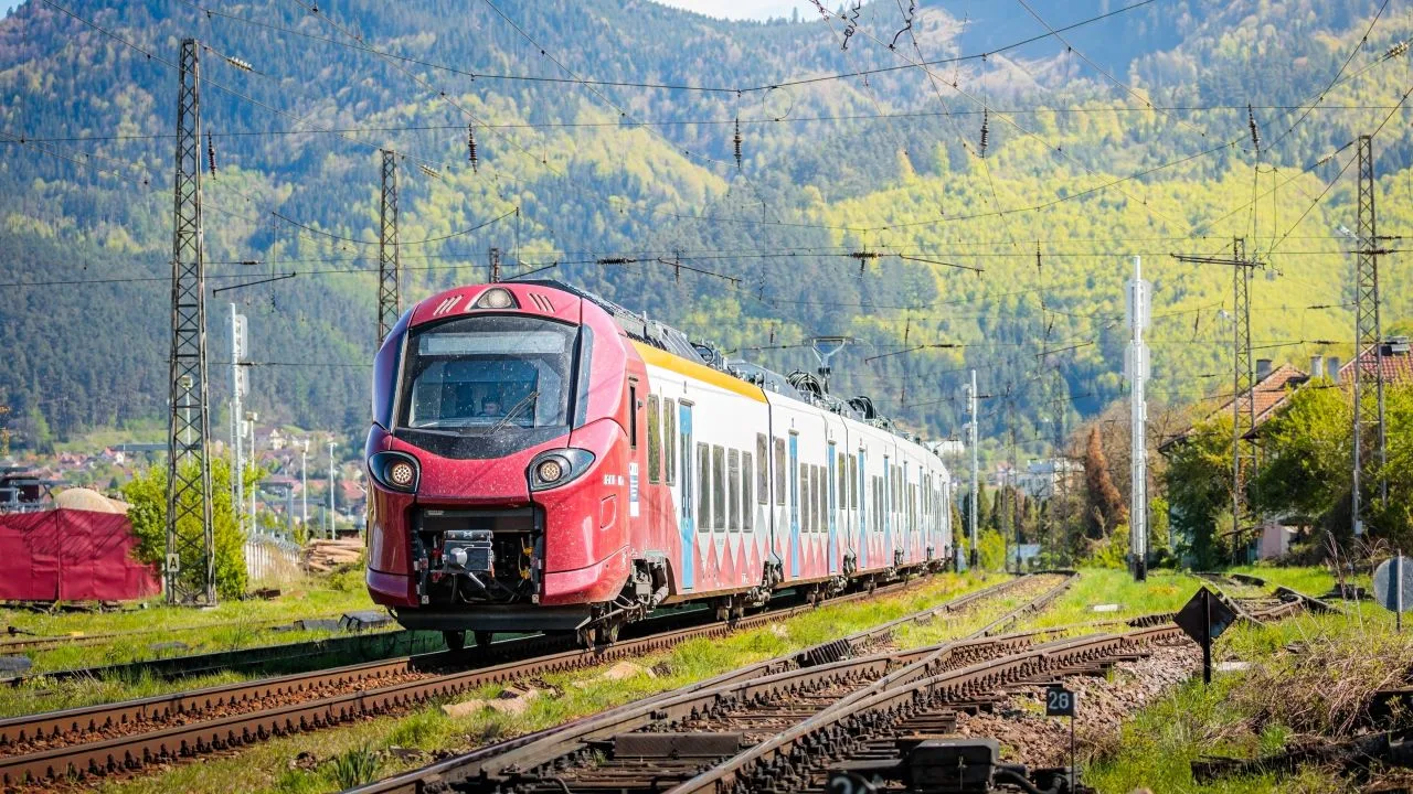 Tren modern pe linia ferată Brașov–Sighișoara în peisaj montan.