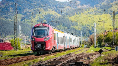 Tren modern pe linia ferată Brașov–Sighișoara în peisaj montan.