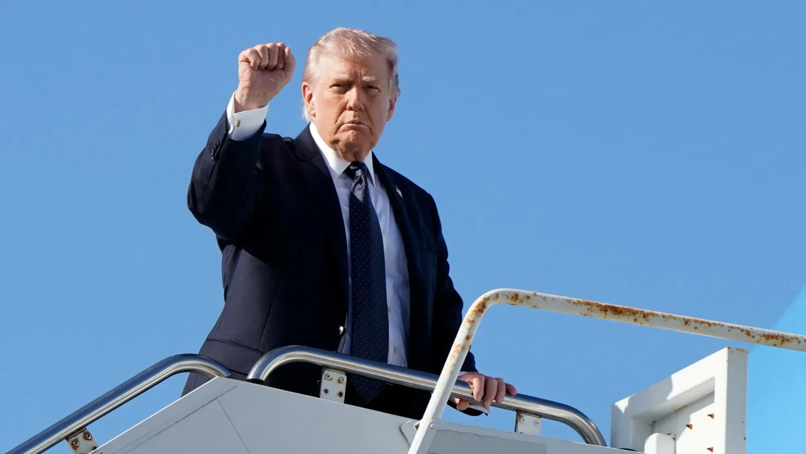 Donald Trump salută de pe scările unui avion, exprimând determinare.