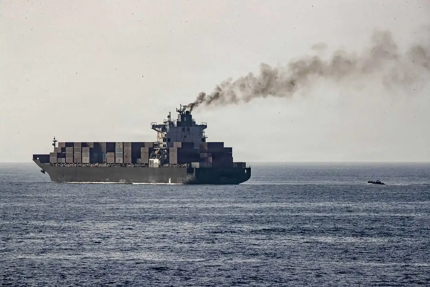 Nava de marfă navigând pe mare, cu fum ieșind din chimenea.