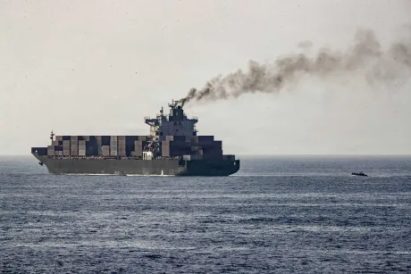Nava de marfă navigând pe mare, cu fum ieșind din chimenea.
