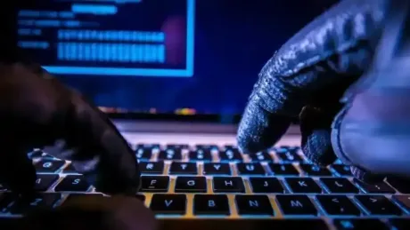 Mâini acoperite cu mănuși tastând pe un laptop.
