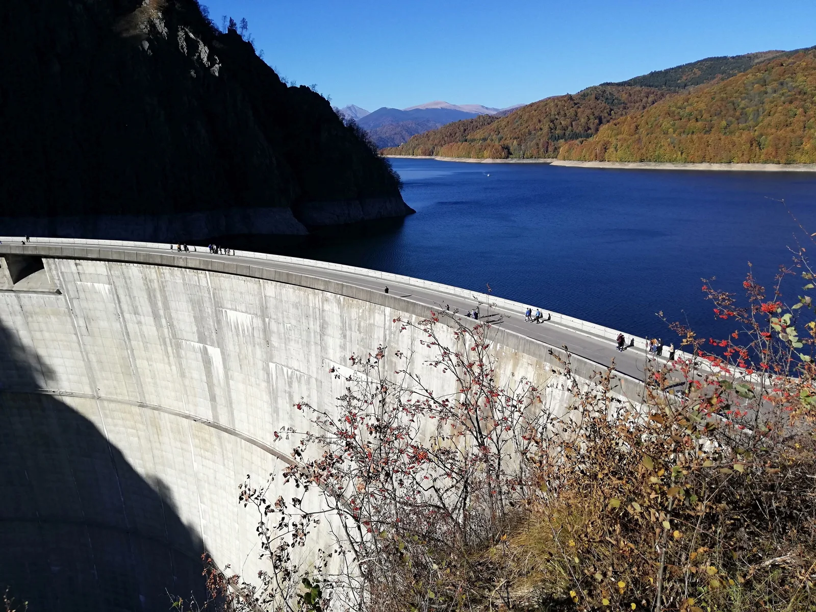 Lacul de acumulare cu nivel scăzut, peisaj montan în fundal, semne de secetă vizibile.