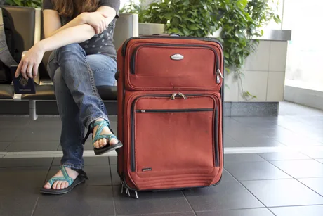 O persoană așezată lângă o valiză roșie într-un aeroport.