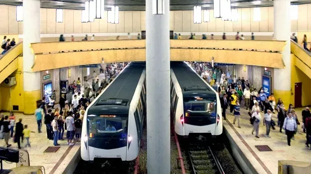 Stație de metrou aglomerată cu trenuri în mișcare.