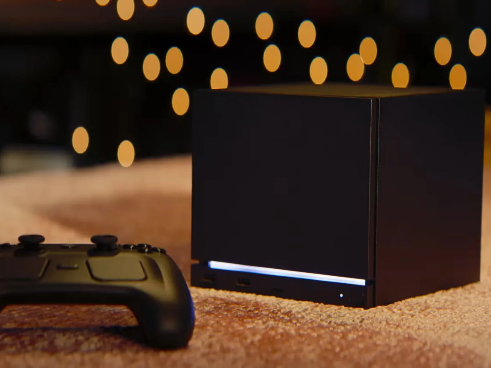 Dispozitiv de gaming negru cu un controller pe un covor, în fundal lumini difuze.
