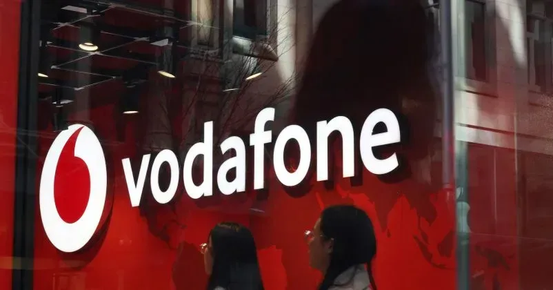 Logo Vodafone România pe fundal roșu, cu clienți în față.