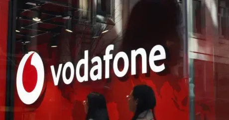 Logo Vodafone România pe fundal roșu, cu clienți în față.