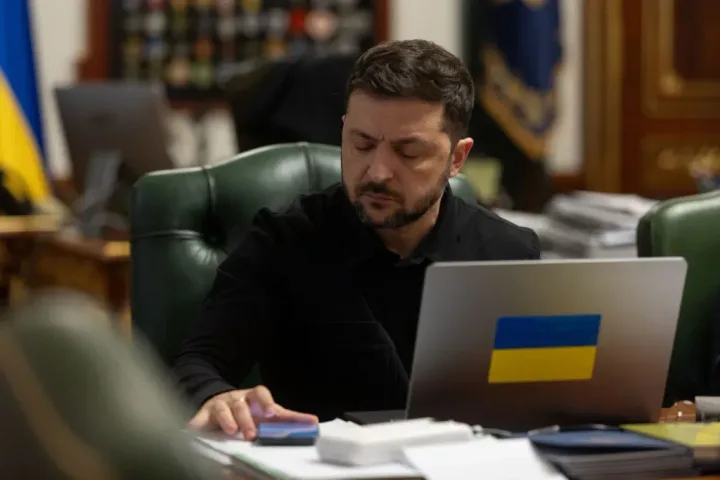 Volodimir Zelenski lucrând la birou, cu steagul Ucrainei pe laptop.