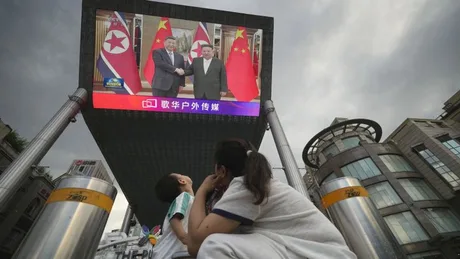 O familie privește un ecran uriaș cu Xi Jinping și Kim Jong Un la Phenian.