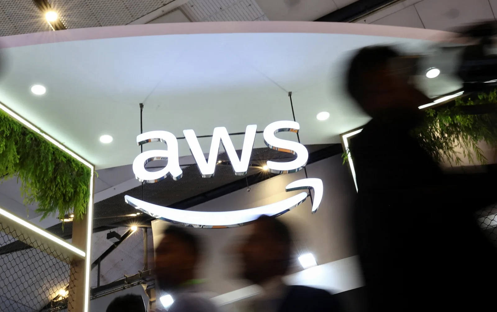 Logo-ul Amazon Web Services la un eveniment, cu oameni în mișcare în fundal.