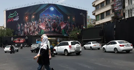 Oameni traversând o stradă aglomerată în fața unui mural impresionant.