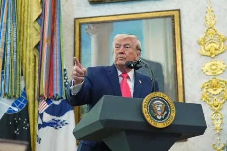 Donald Trump vorbește la un podium, cu steagul în fundal.