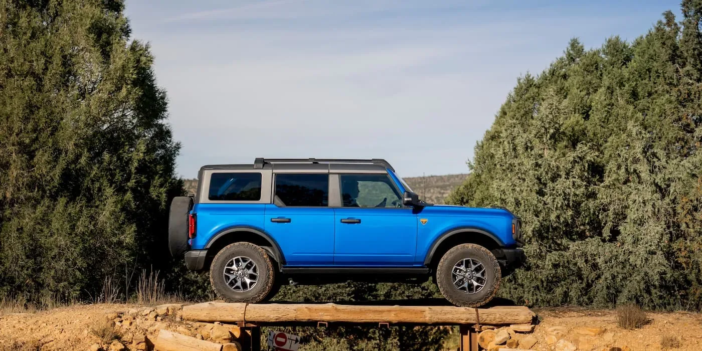 Un model Ford Bronco albastru pe un teren accidentat, înconjurat de vegetație.