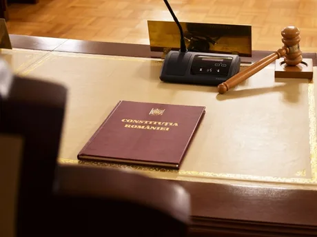 O carte a Constituției României pe un birou de lucru, alături de un ciocan de judecător.