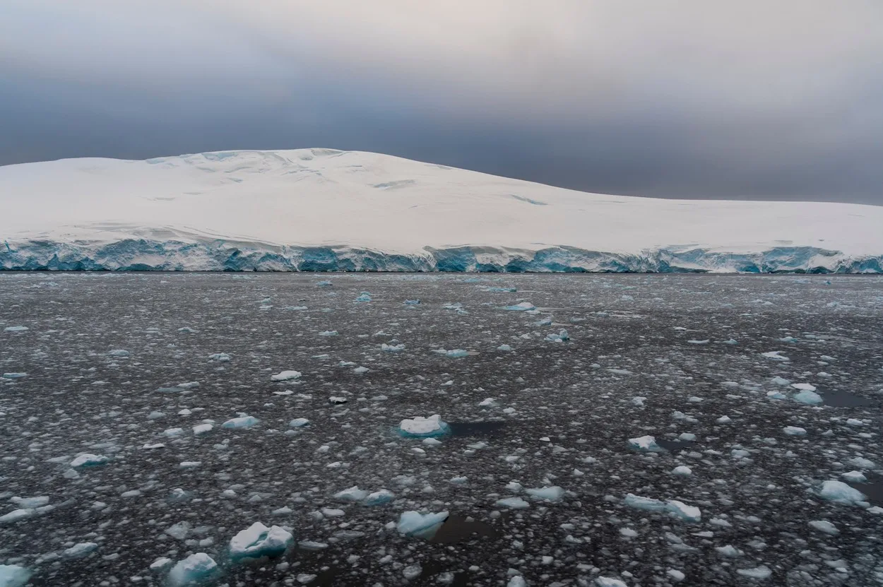 Peisaj de gheață în Antarctica, cu ape deschise și nori întunecați.