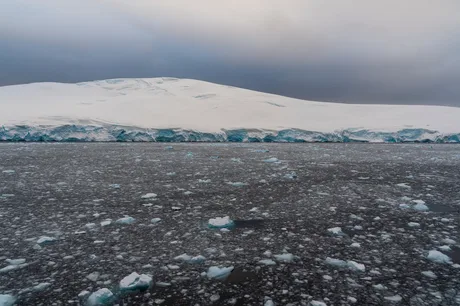 Peisaj de gheață în Antarctica, cu ape deschise și nori întunecați.
