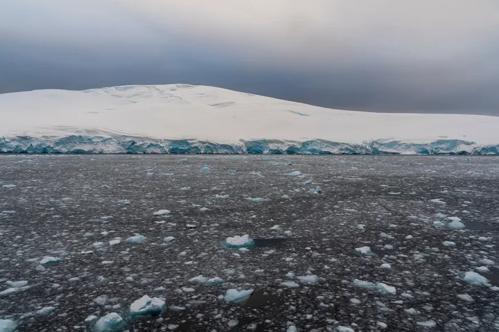 Peisaj de gheață în Antarctica, cu ape deschise și nori întunecați.
