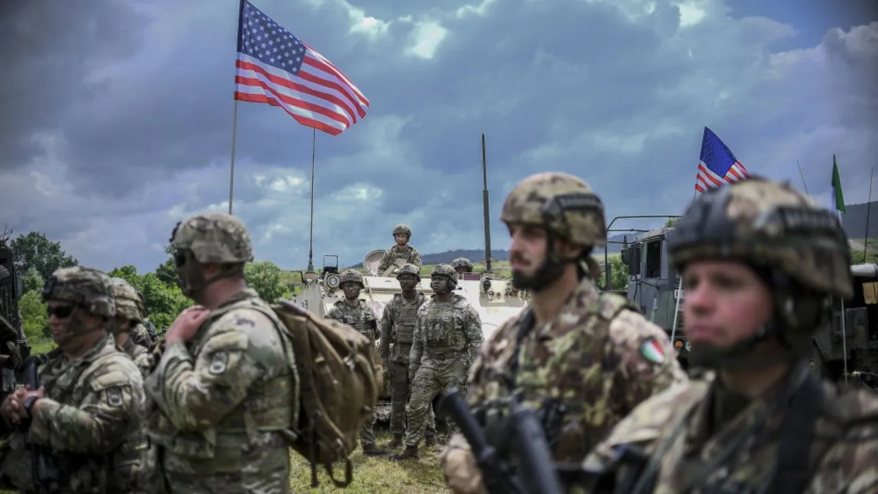 Soldați americani și italieni în exercițiu militar, cu steaguri în fundal.