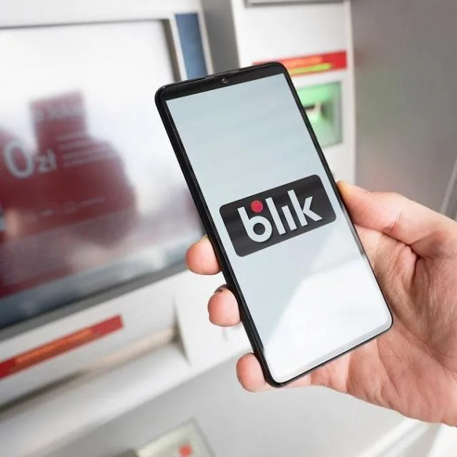 Un telefon mobil care afișează logo-ul BLIK la un ATM.